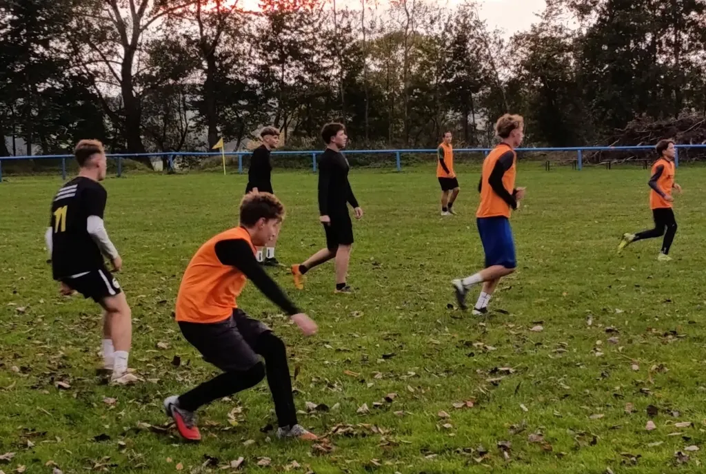 Fotbalisté v oranžových a černých dresech běhají po hřišti při rozcvičce.