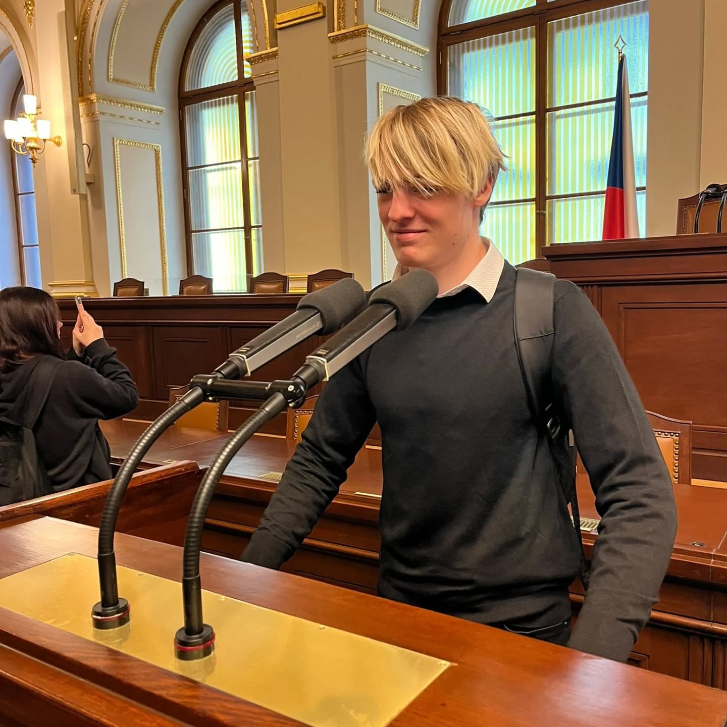 Student stojí u řečnického pultu s mikrofony v jednacím sále Poslanecké sněmovny.