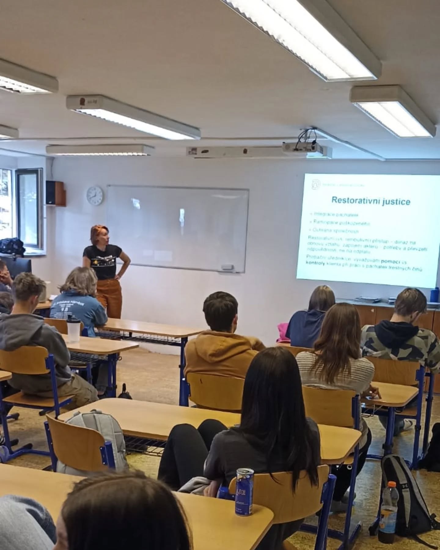 Přednášející popisuje téma restorativní justice studentům v učebně u promítané prezentace.