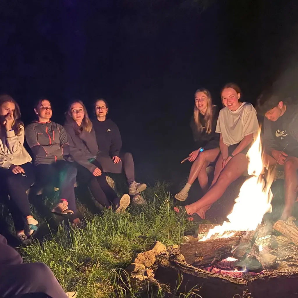 Studenti sedí v kruhu kolem hořícího ohně za tmy během večerního výletu.