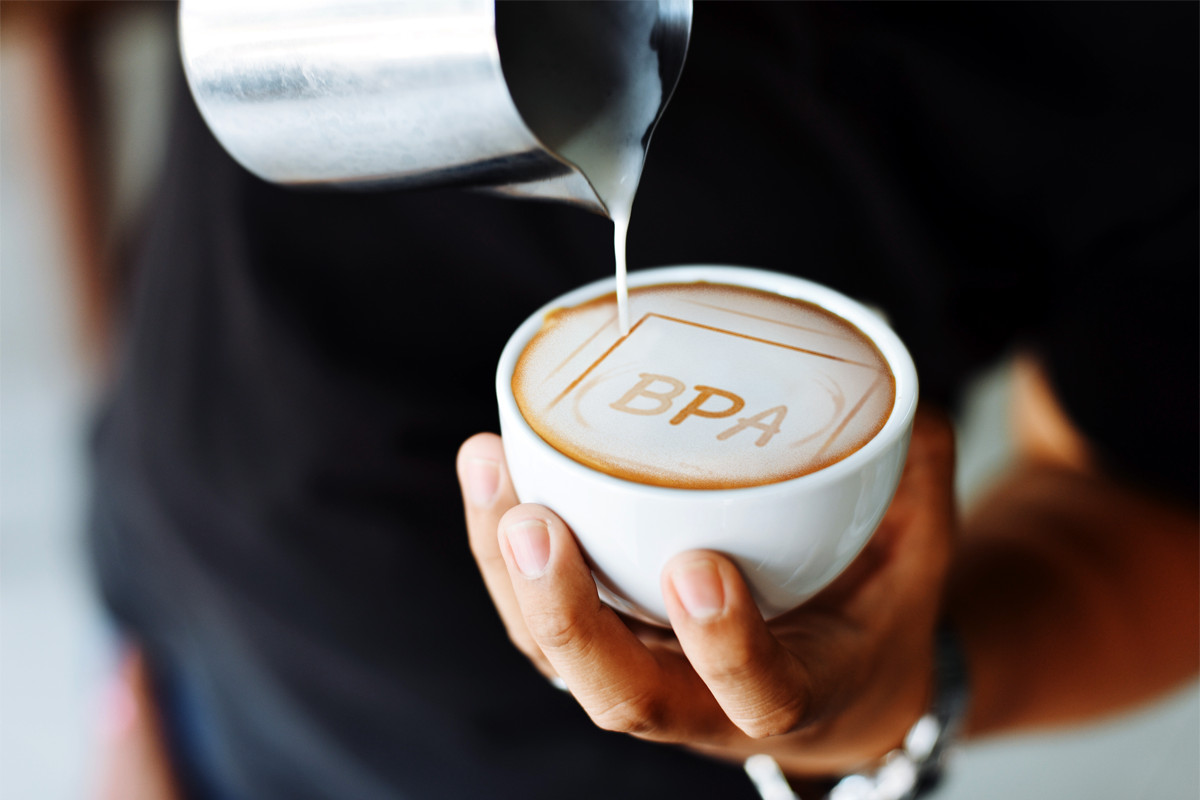 Barista nalévá mléko do kávy s motivem nápisu BPA ve pěně.