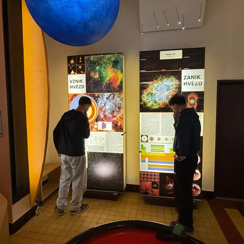 Žáci si prohlížejí výstavní panely o vzniku a zániku hvězd v planetáriu.