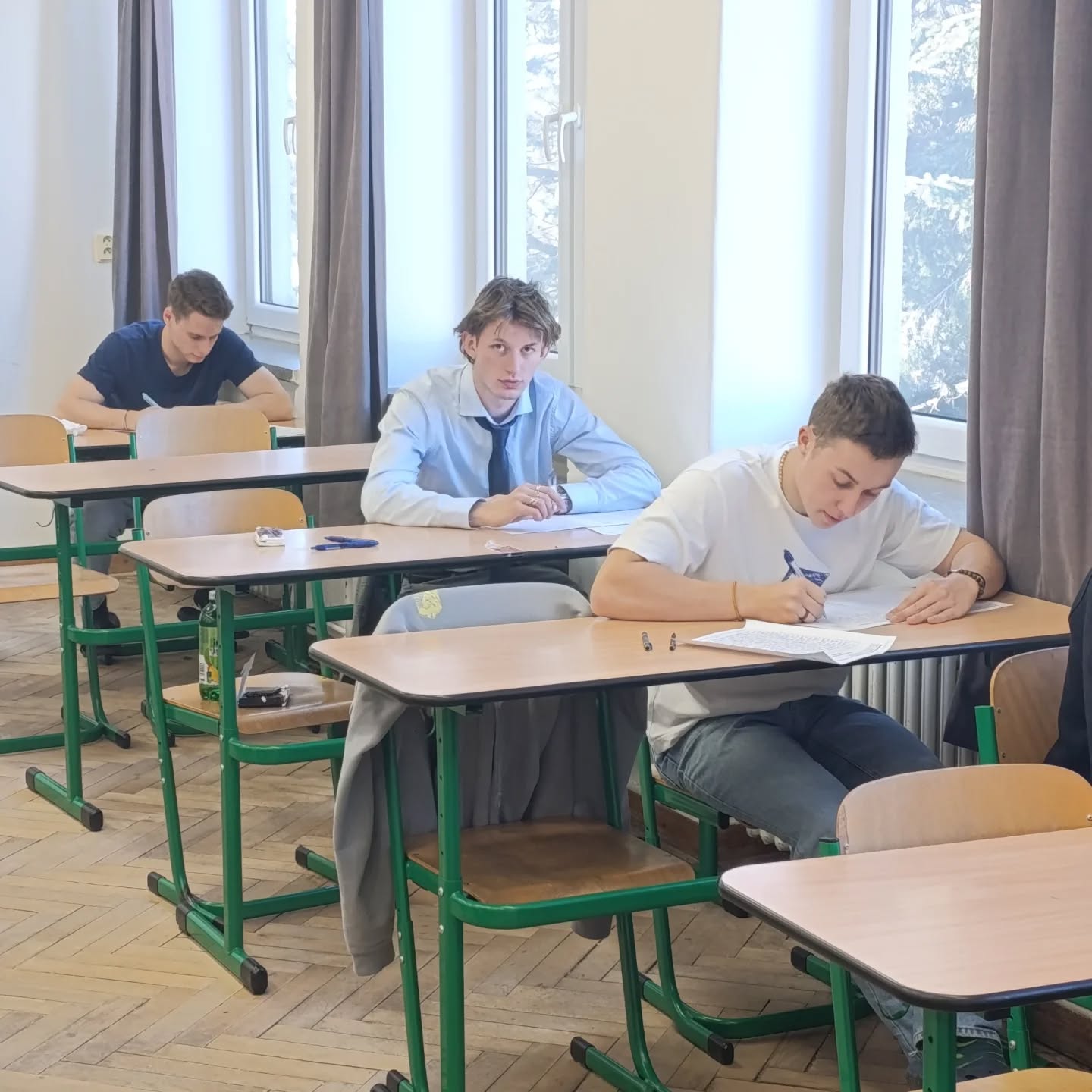 Žáci píší písemnou maturitní zkoušku v lavicích učebny.