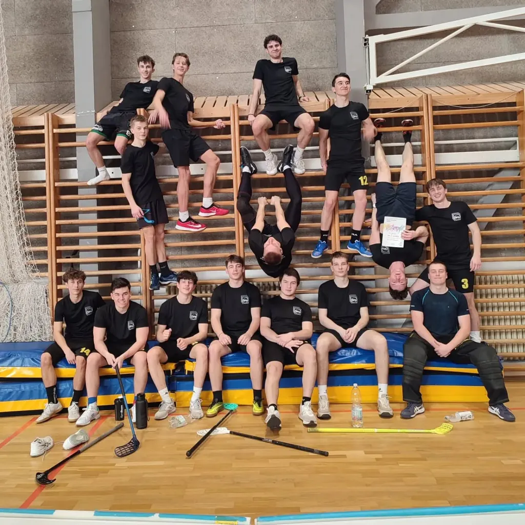 Chlapecký florbalový tým pózuje na žebřinách a lavičce ve sportovní hale.