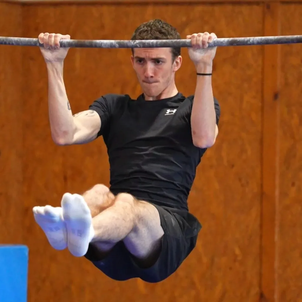 Mladý sportovec cvičí na hrazdě se skrčenými koleny při gymnastickém cviku.